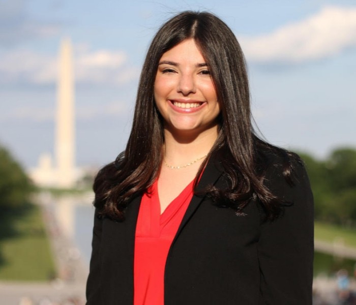 A student smiling in front of the Washington Monument and reflecting pool.