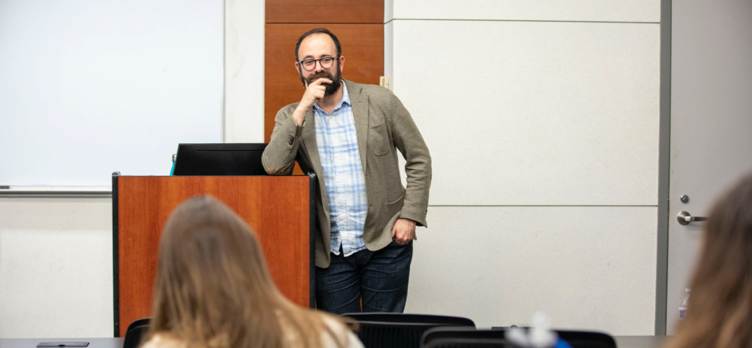 A faculty member stands near a lectern during a lecture class.