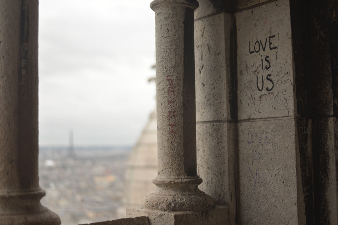 Love is us graffiti on column with Paris city scape in distance