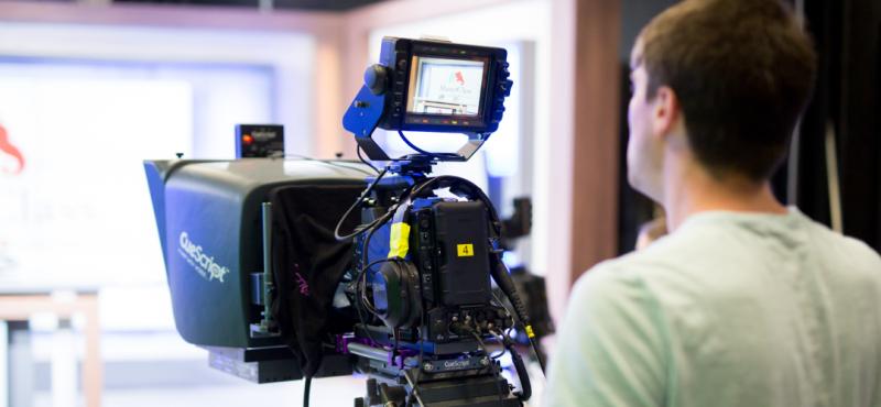 A person uses a news room camera to film a video.