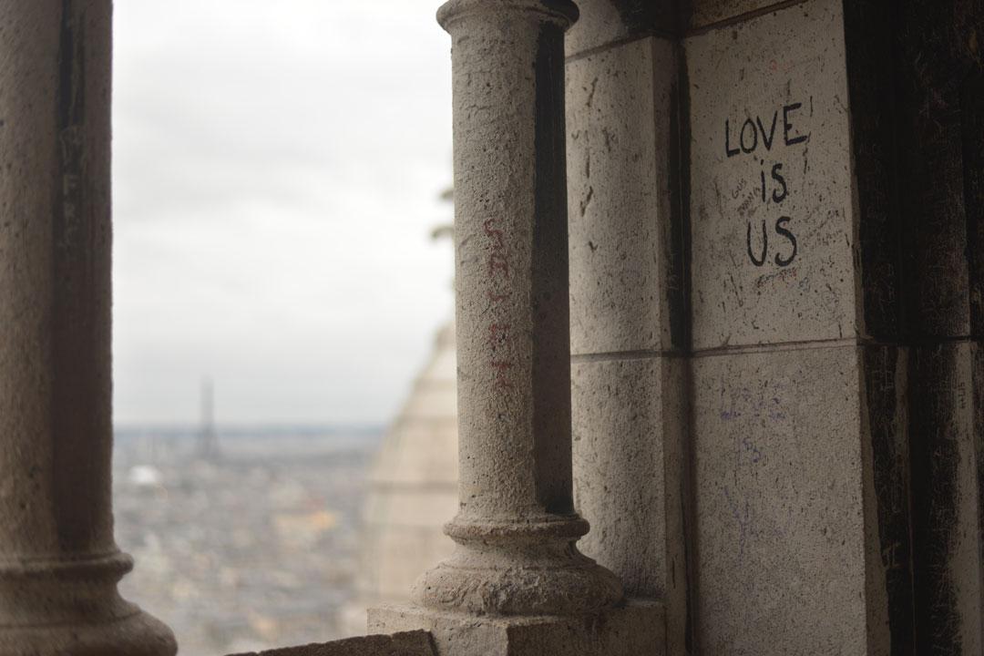 Love is us graffiti on column with Paris city scape in distance